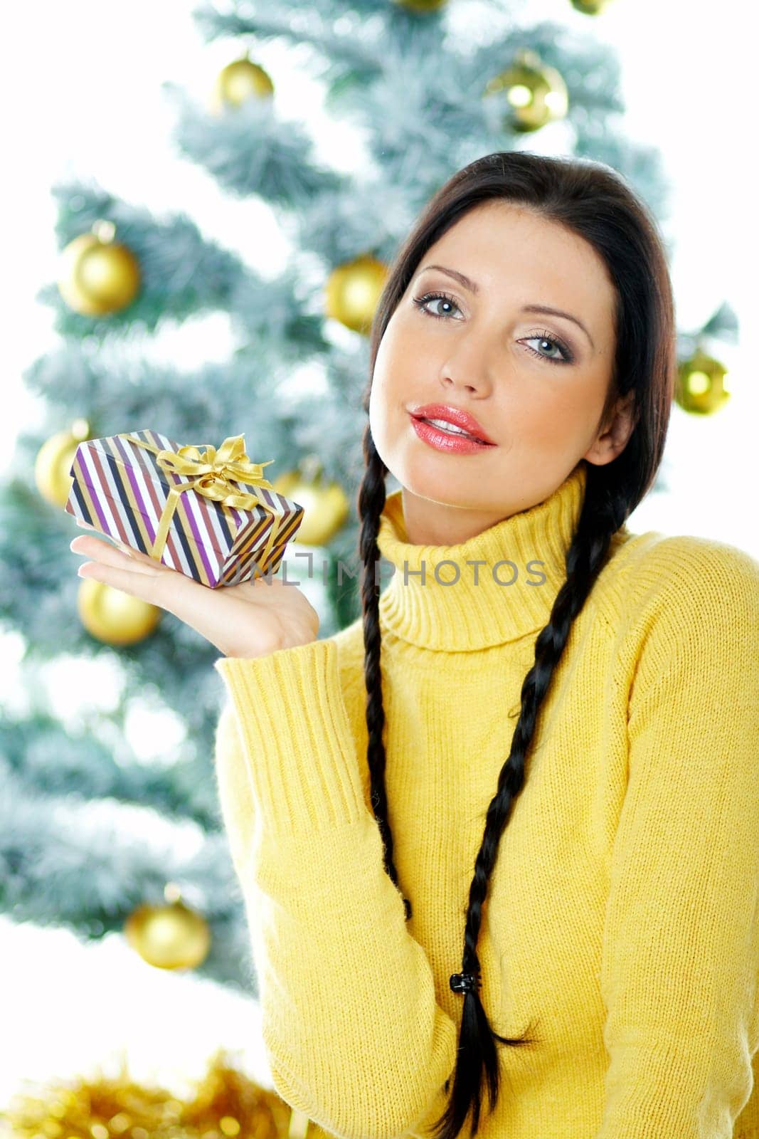 Beautiful brunette woman next to christmas tree on white background holding boxed gift