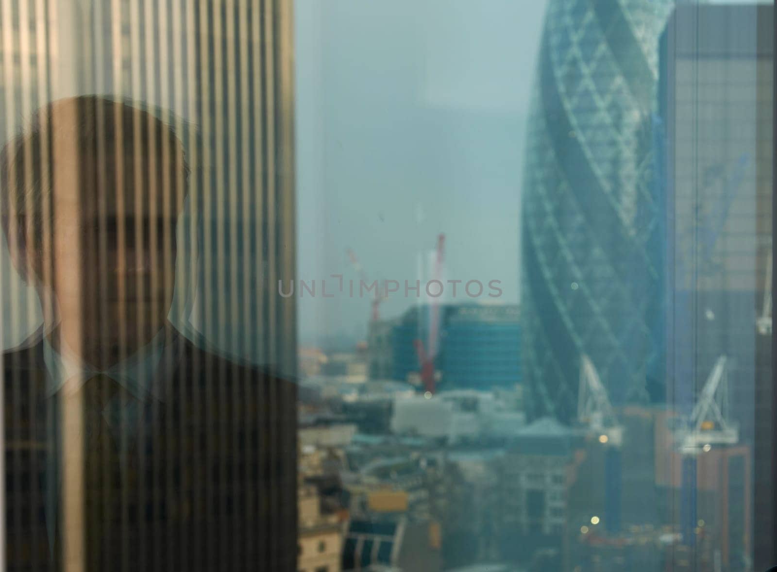 reflection of business man in window with view of London city district in background