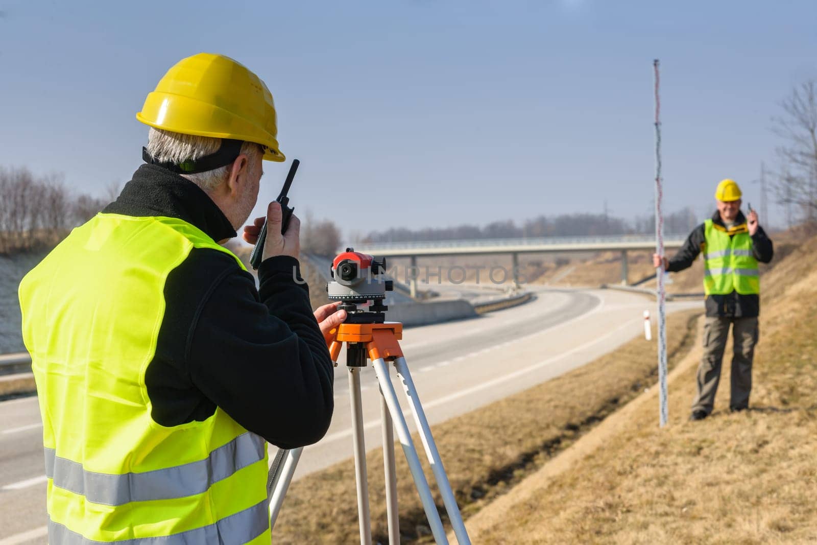 Land surveyors measuring with tacheometer speaking through transmitter highway
