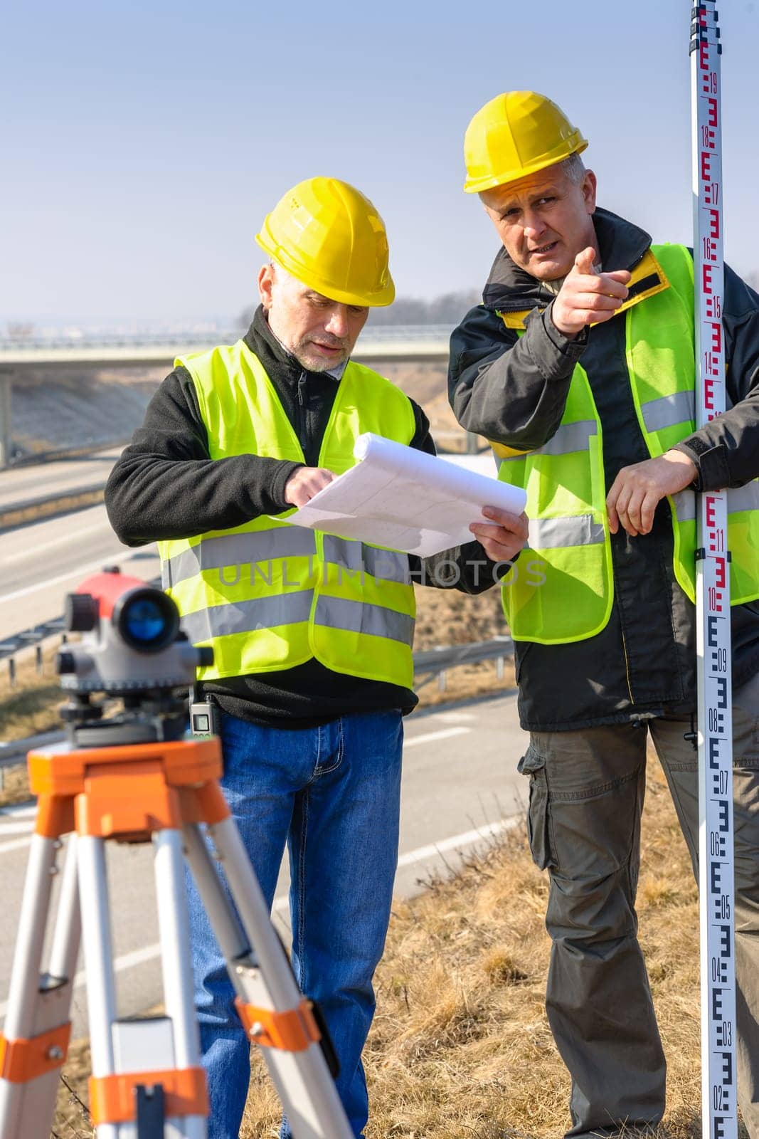 Land surveyors on highway reading geodesist plans use tacheometer