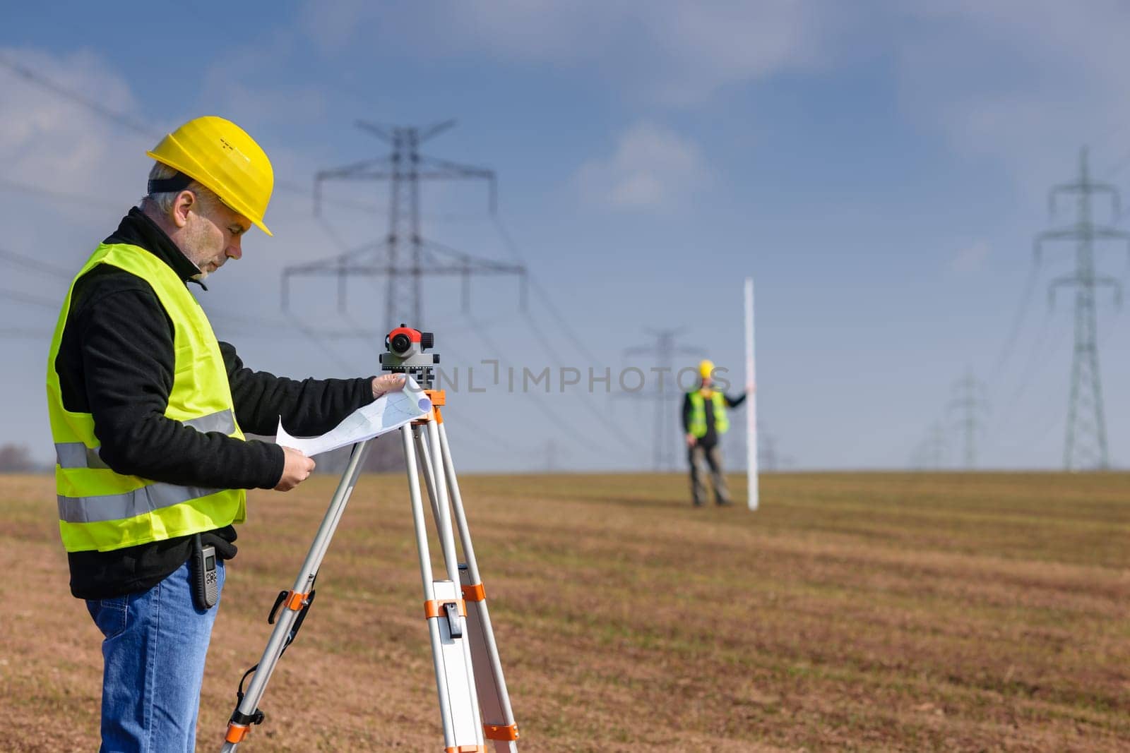 Land surveyors on construction site reading plans wear reflective clothing