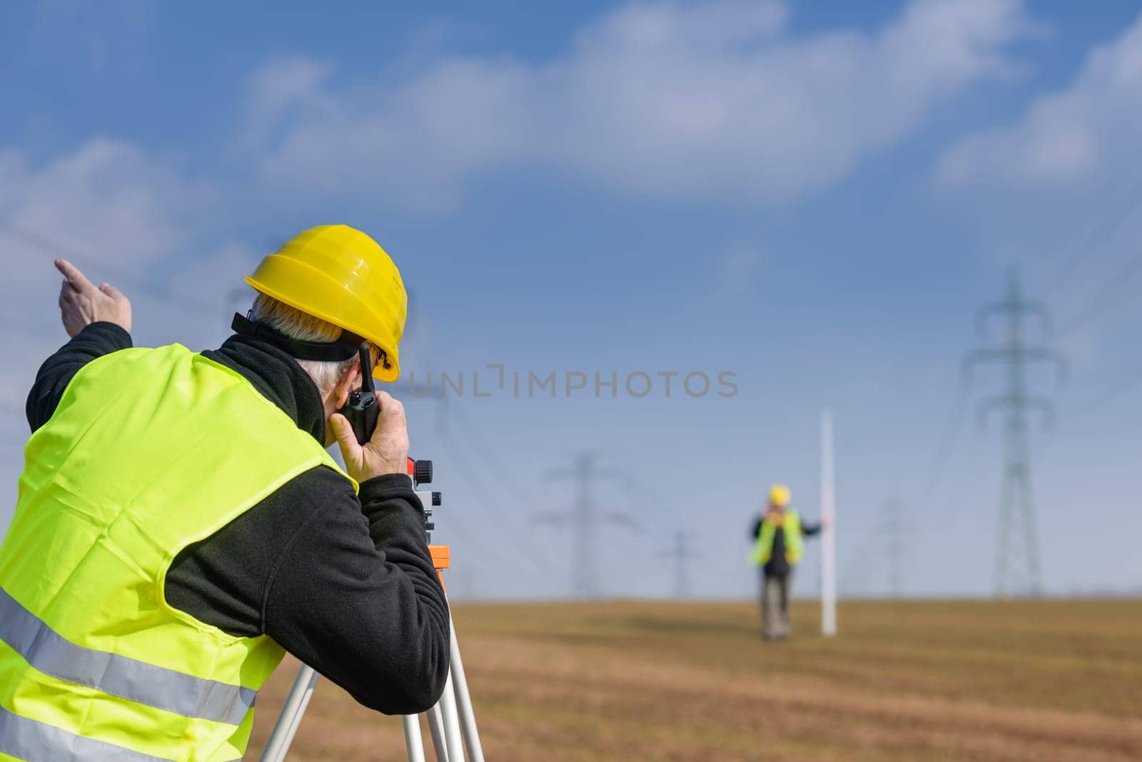 Land surveyors measuring with tacheometer speaking through transmitter construction site