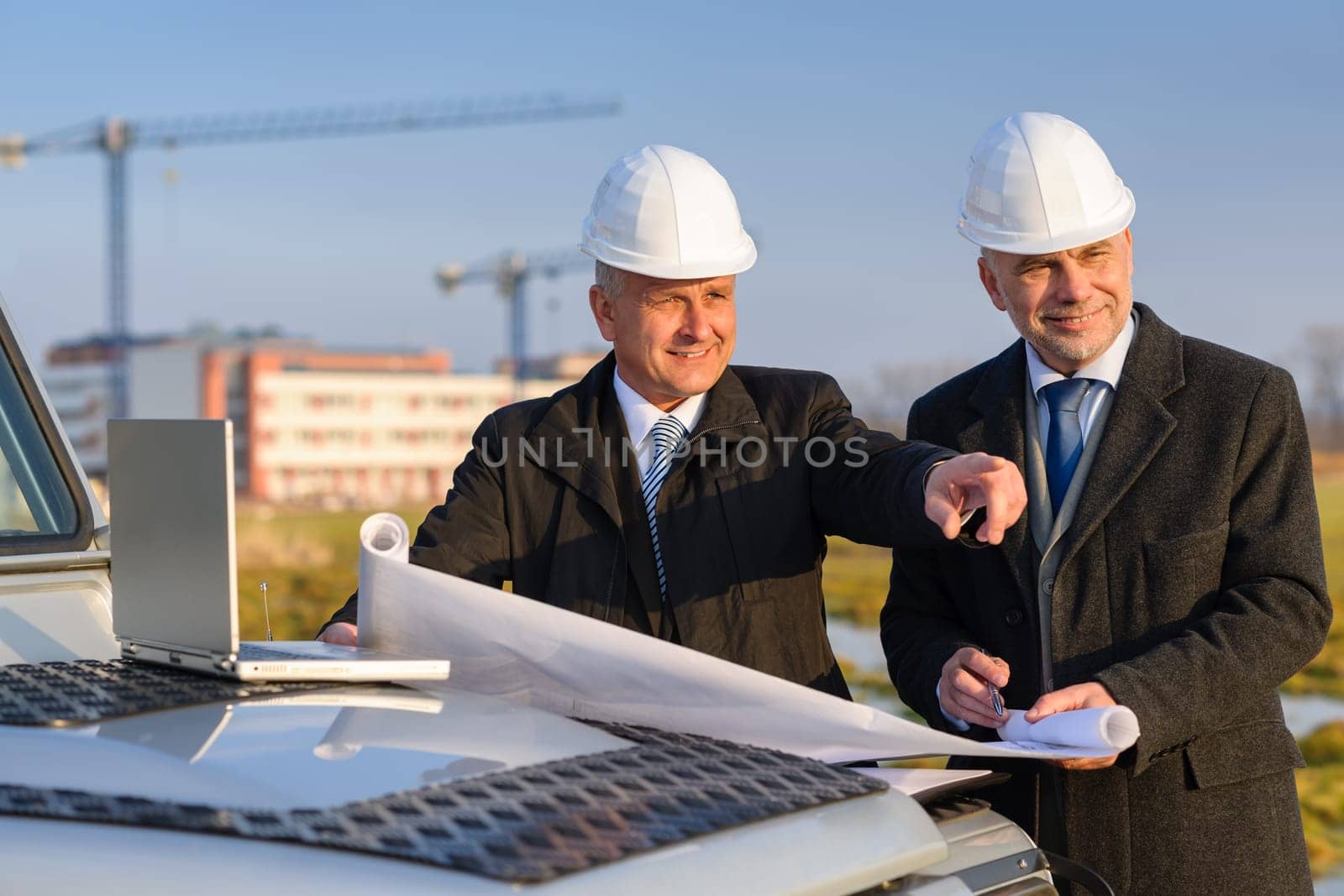 Male developers with blueprints at construction site discuss architect project