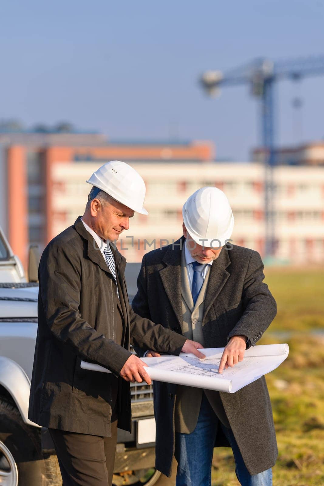 Two senior architect developers review plans at a construction site