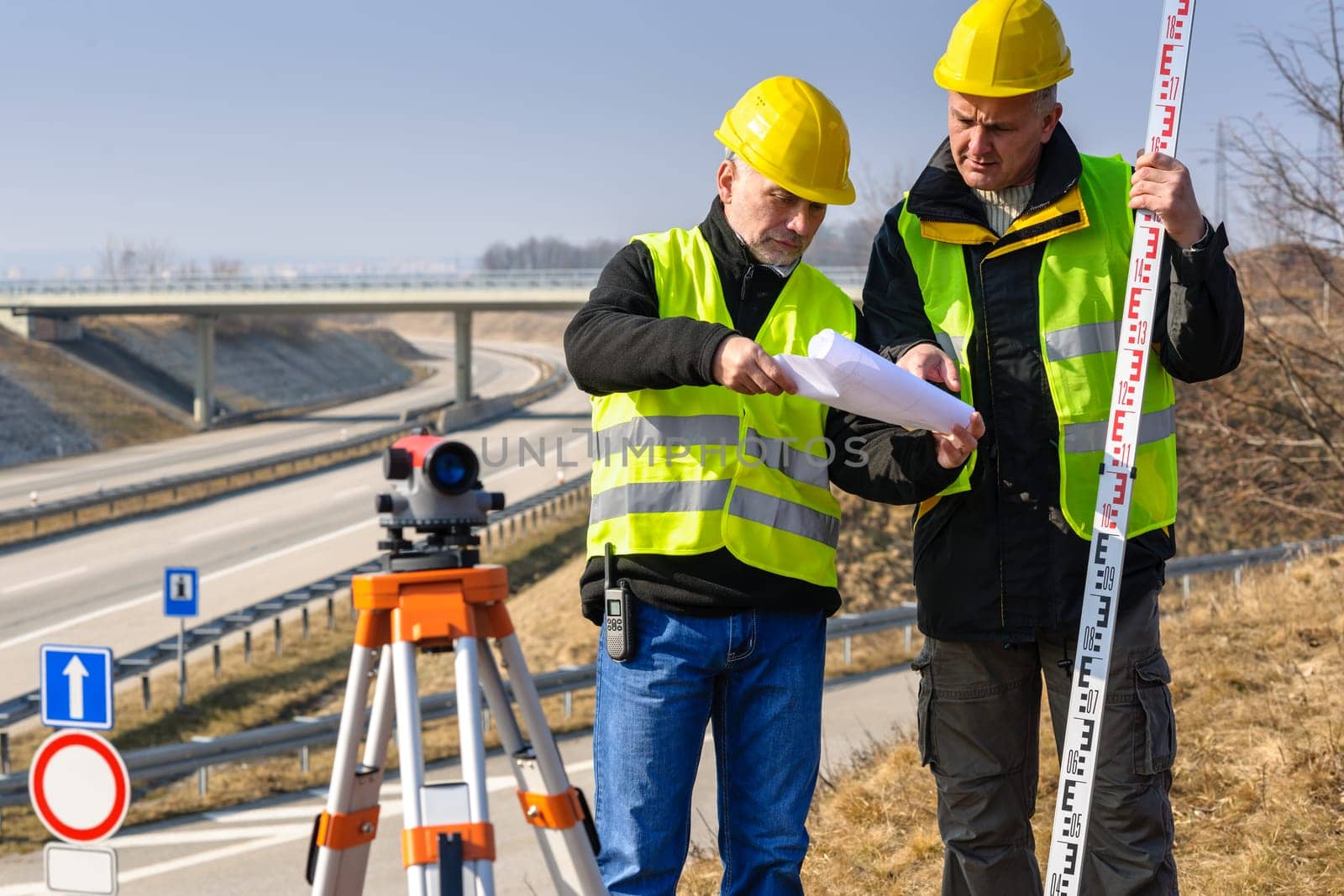 Land surveyors on highway reading geodesist plans use tacheometer