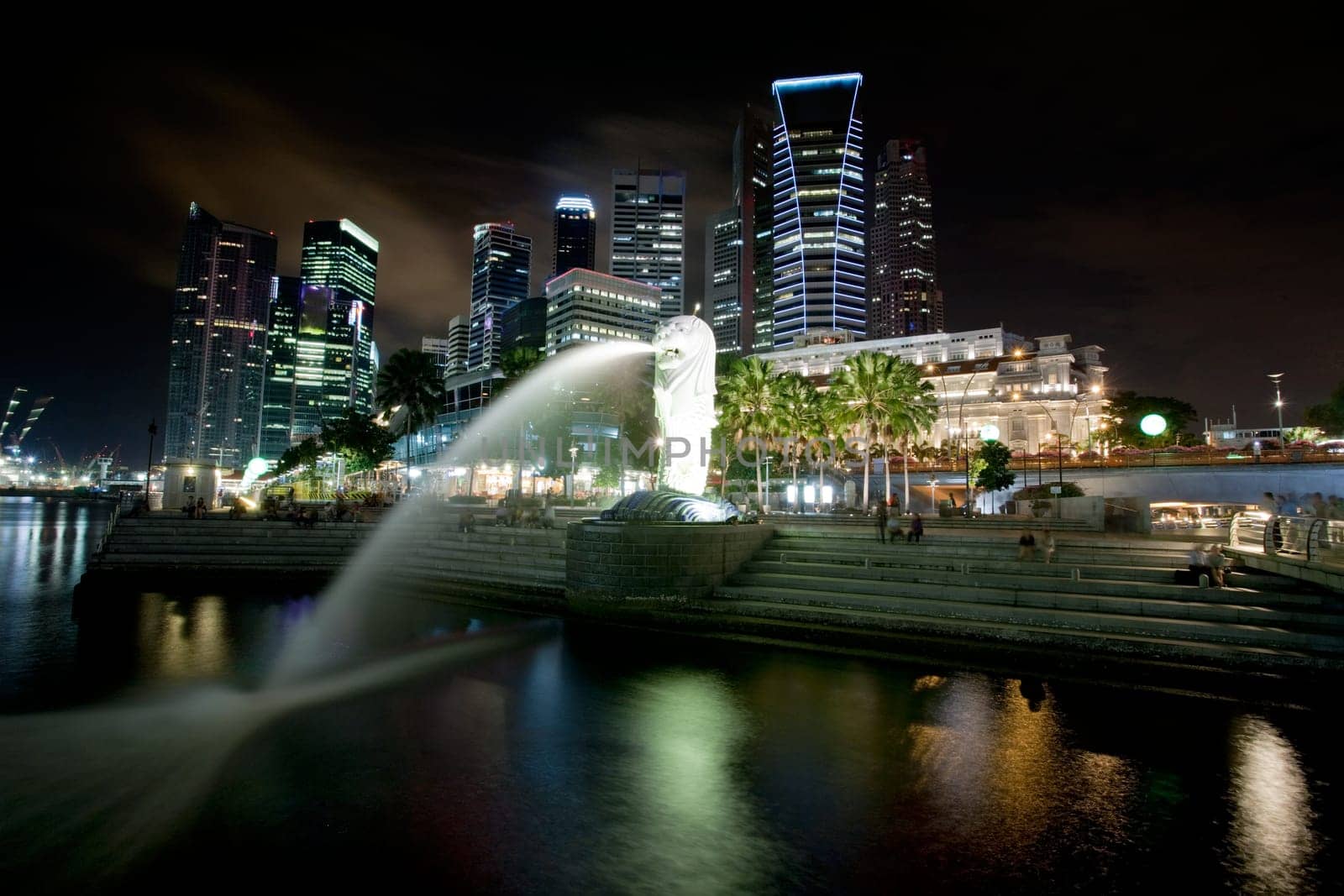 A view of singapore at night with the merlion in the foreground