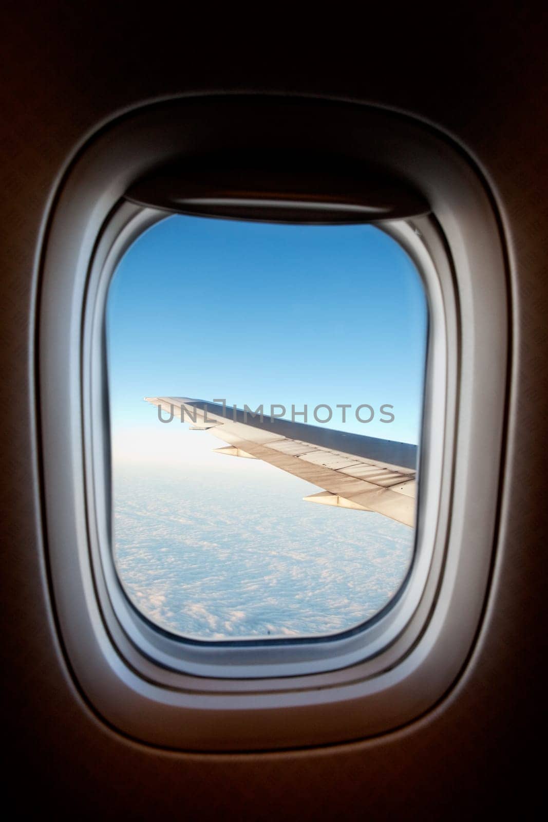 An airplane window with wing and cloudscape