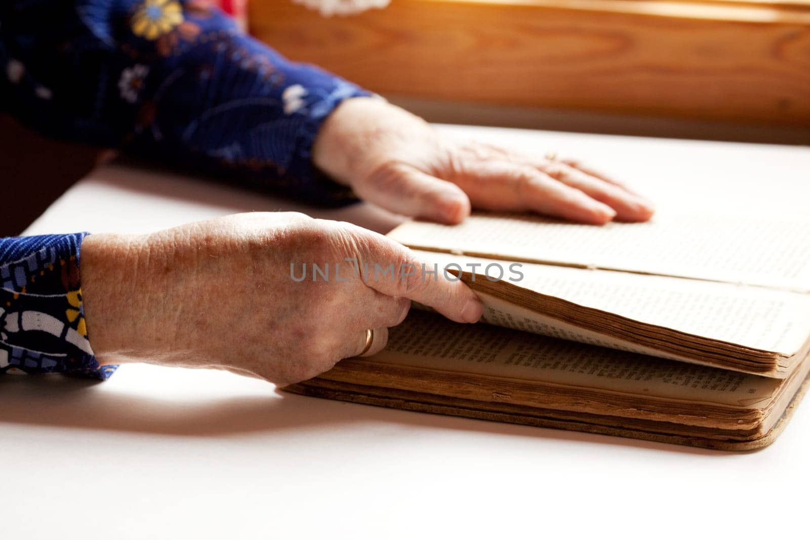 An old pair of hands holding the pages in a book, reading.