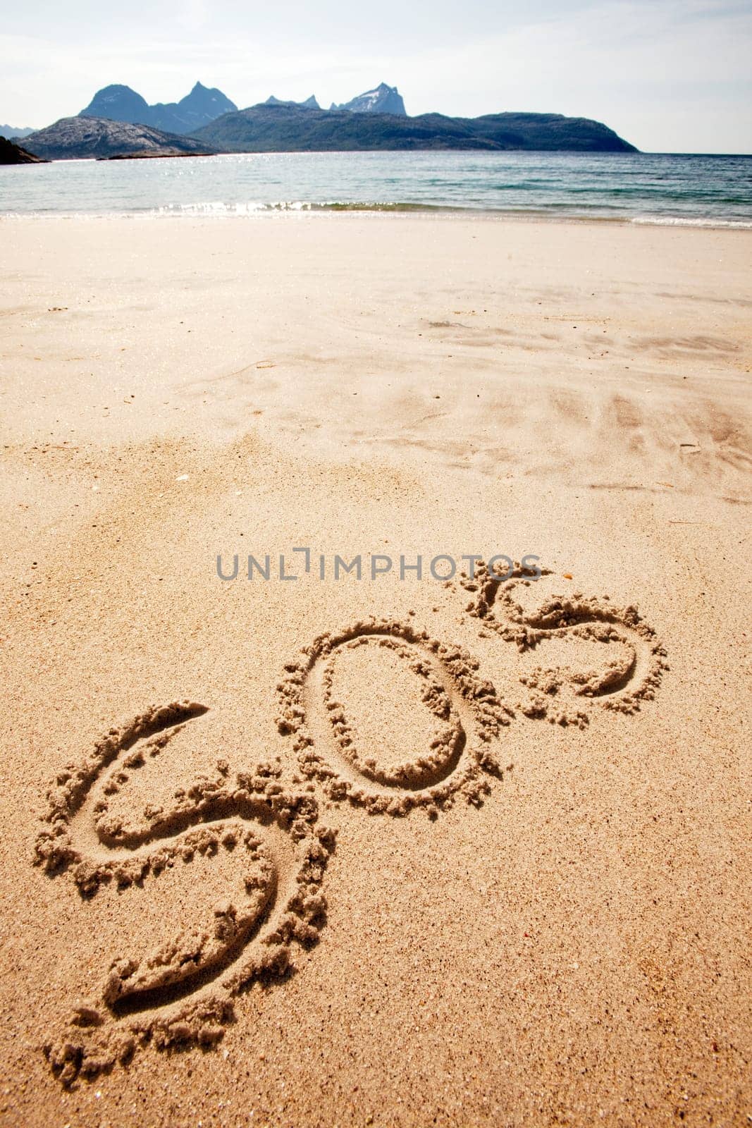 S.O.S written in the sand of an island with the ocean in the distance