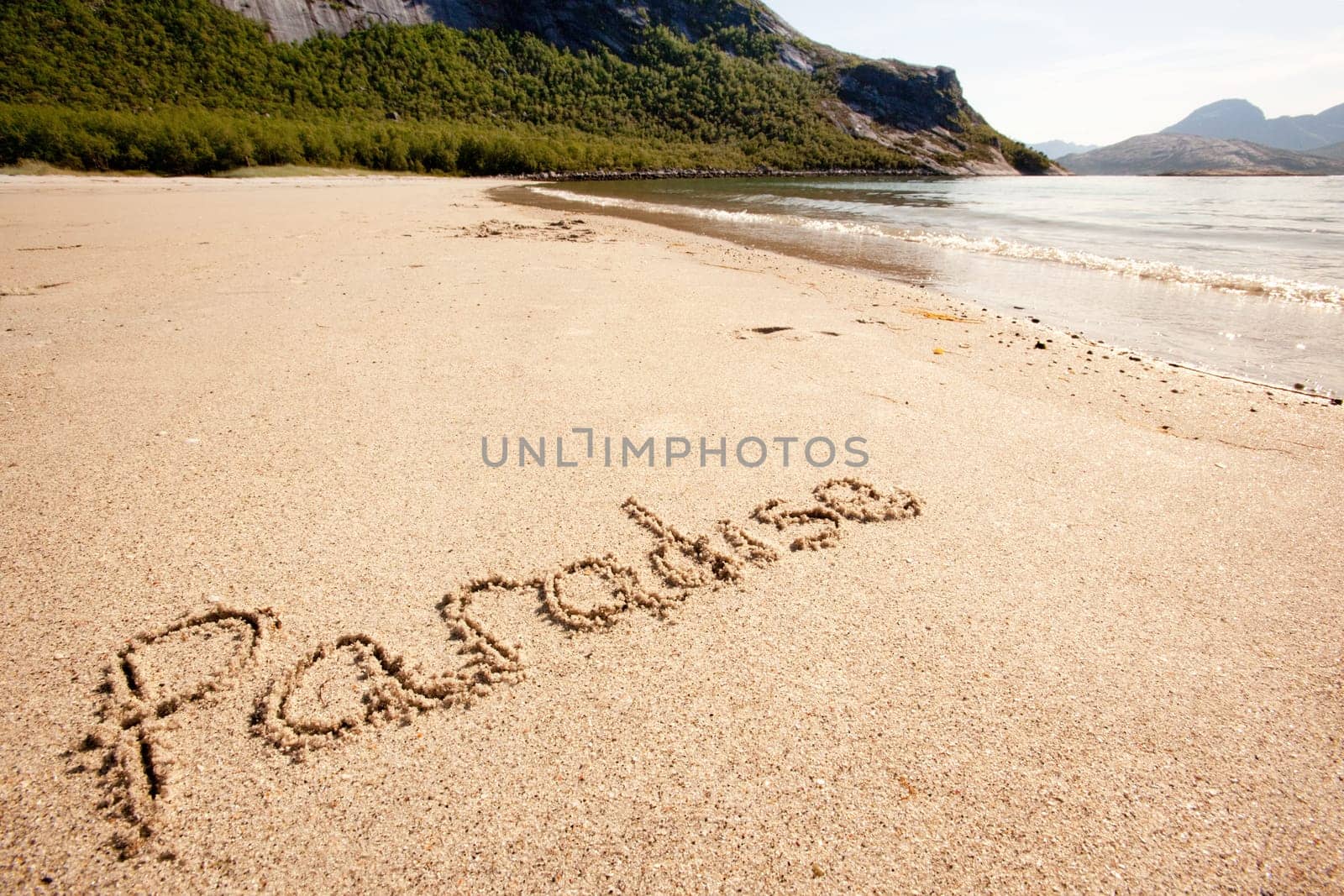 The word paradise written in the sand on a beautiful island