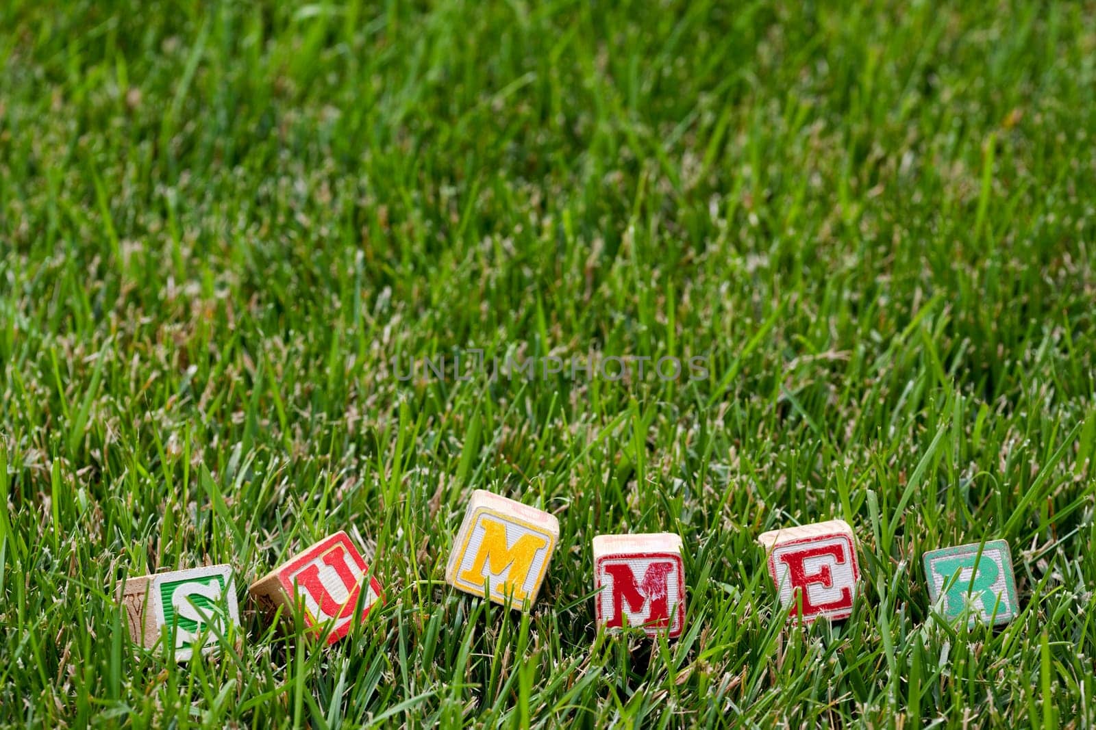 Wooden baby block spelling the word summer in grass