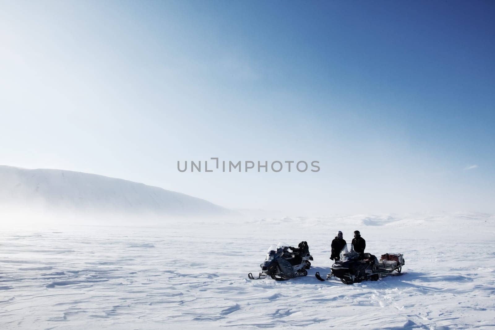 Three snowmobiles on a winter landscape with blowing snow