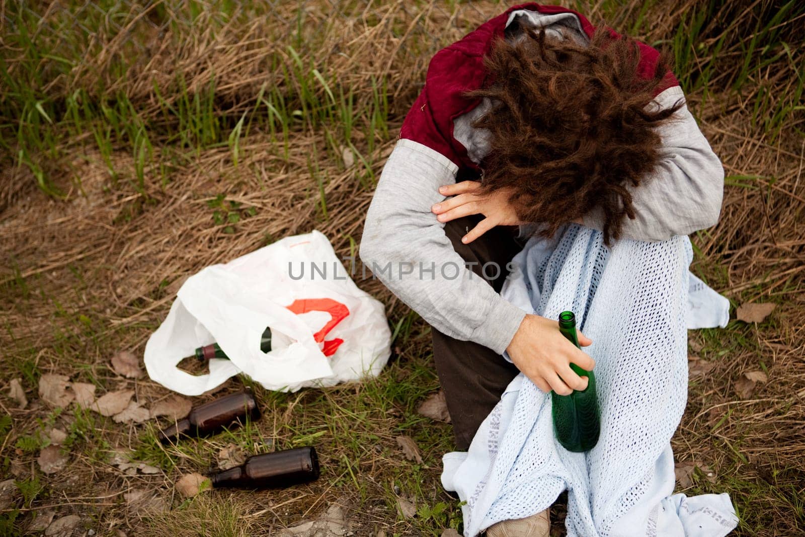 A drunk person sitting in a ditch with a wine bottle