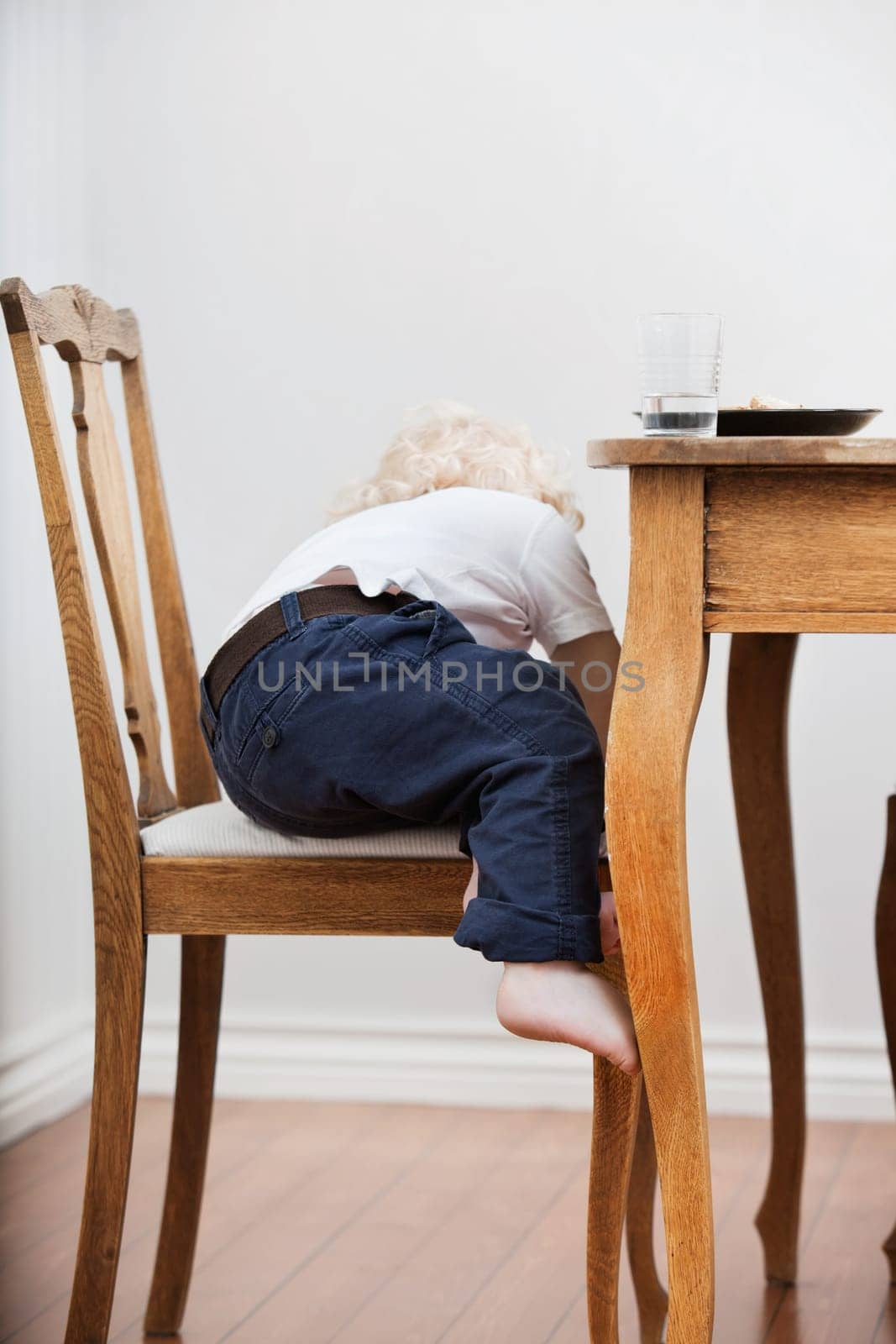 Cute blond child trying to get down from chair near dining table