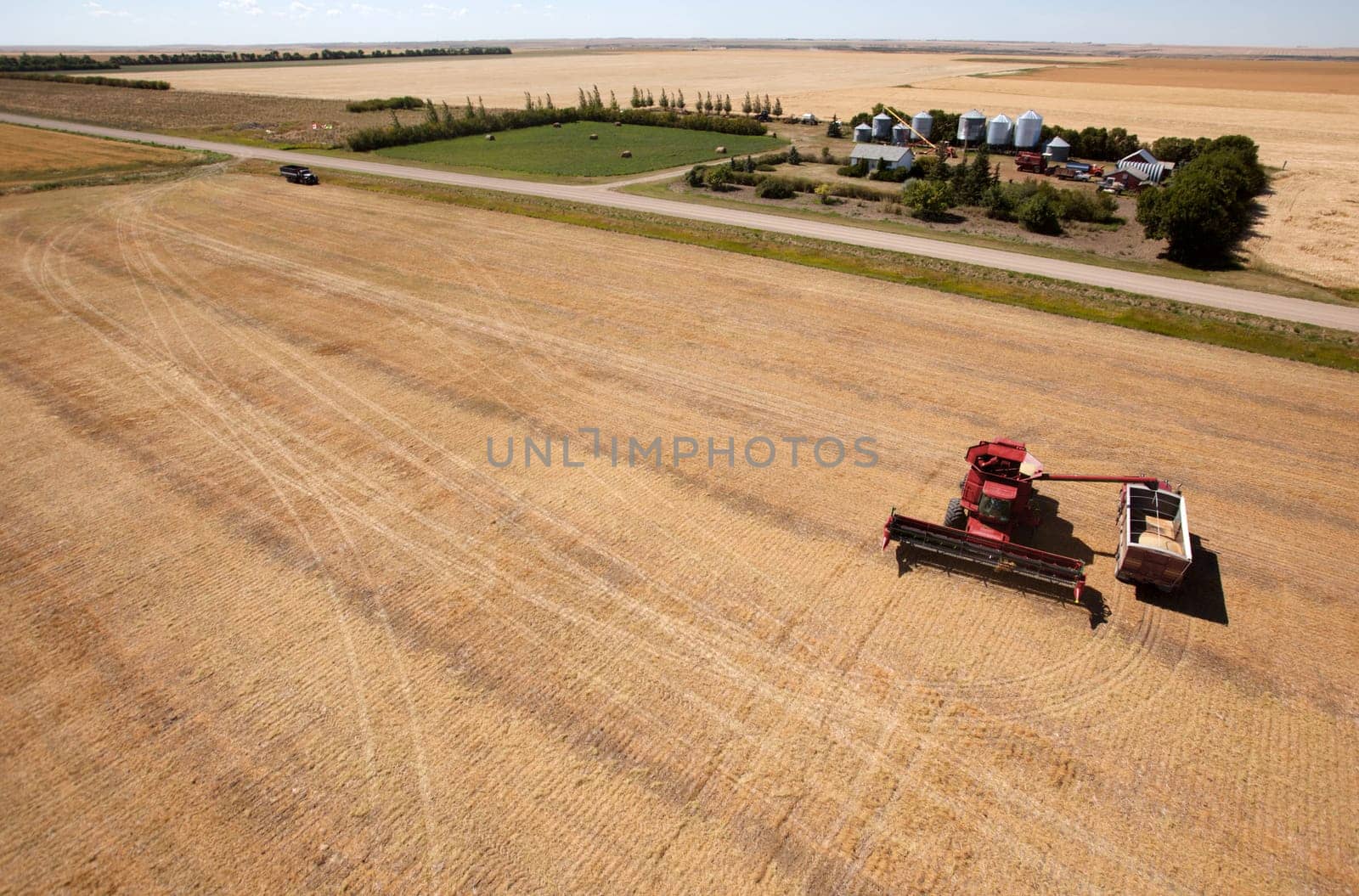 A harvester filling a grain truck with farm yard in background