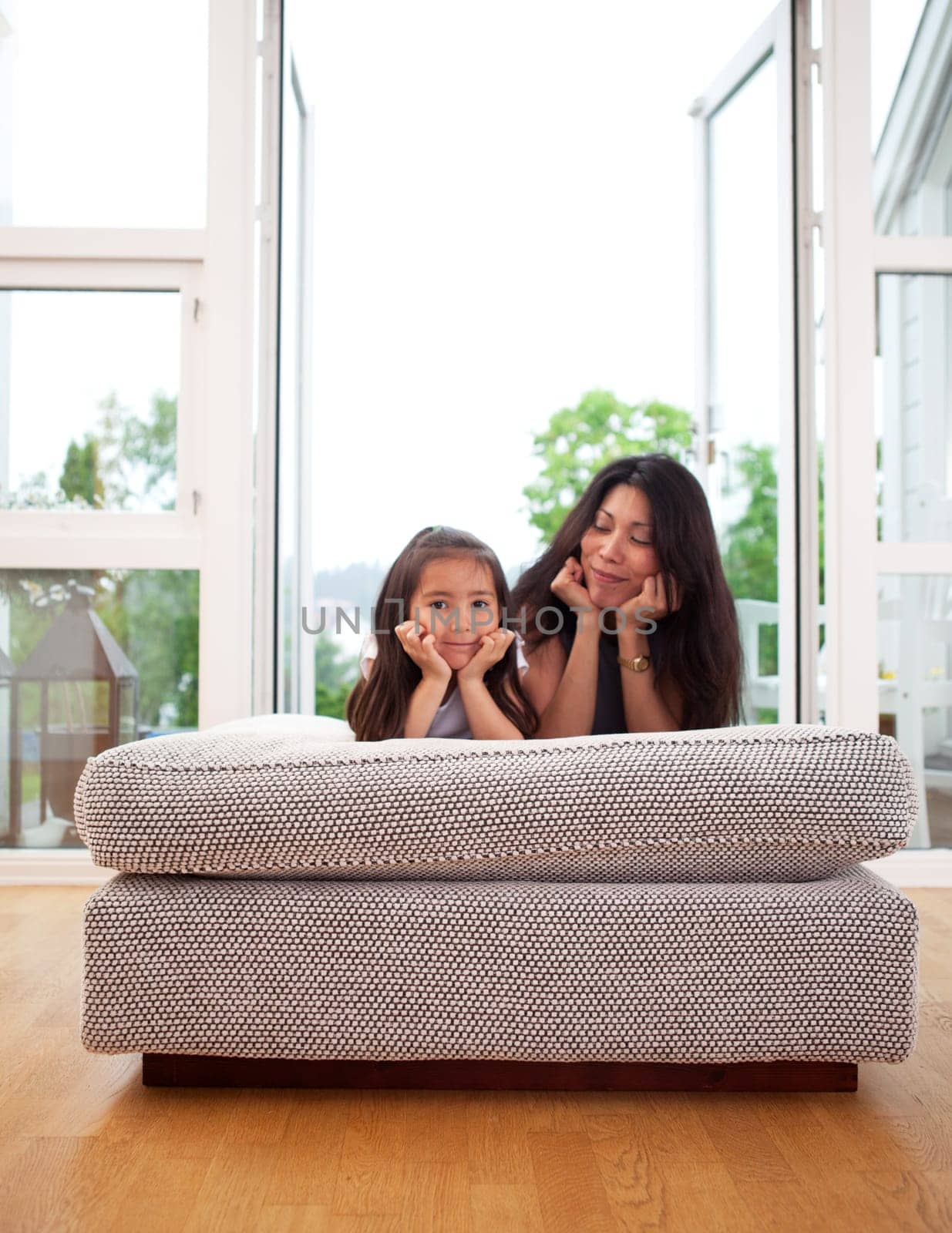 Happy mother and daughter sitting on a couch cushion with a smile, mother looking lovingly at daughter