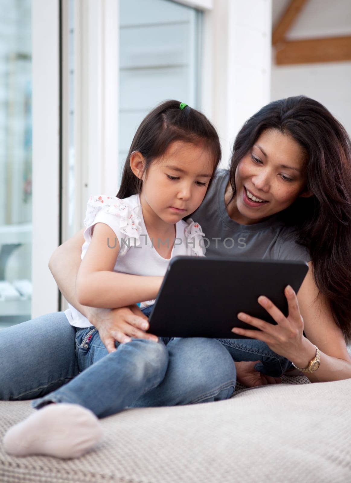 A cute happy mother and daughter using a digital tablet at home in the living room