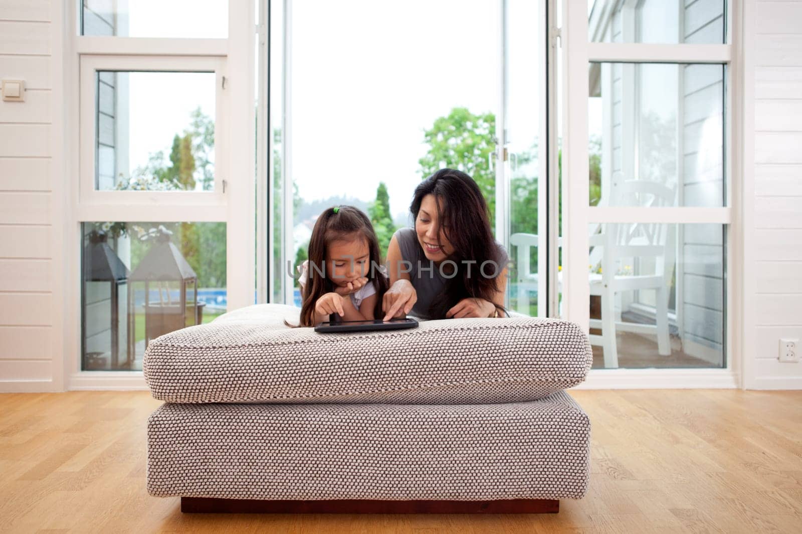 Mother and young daughter using a digital tablet in a living room interior