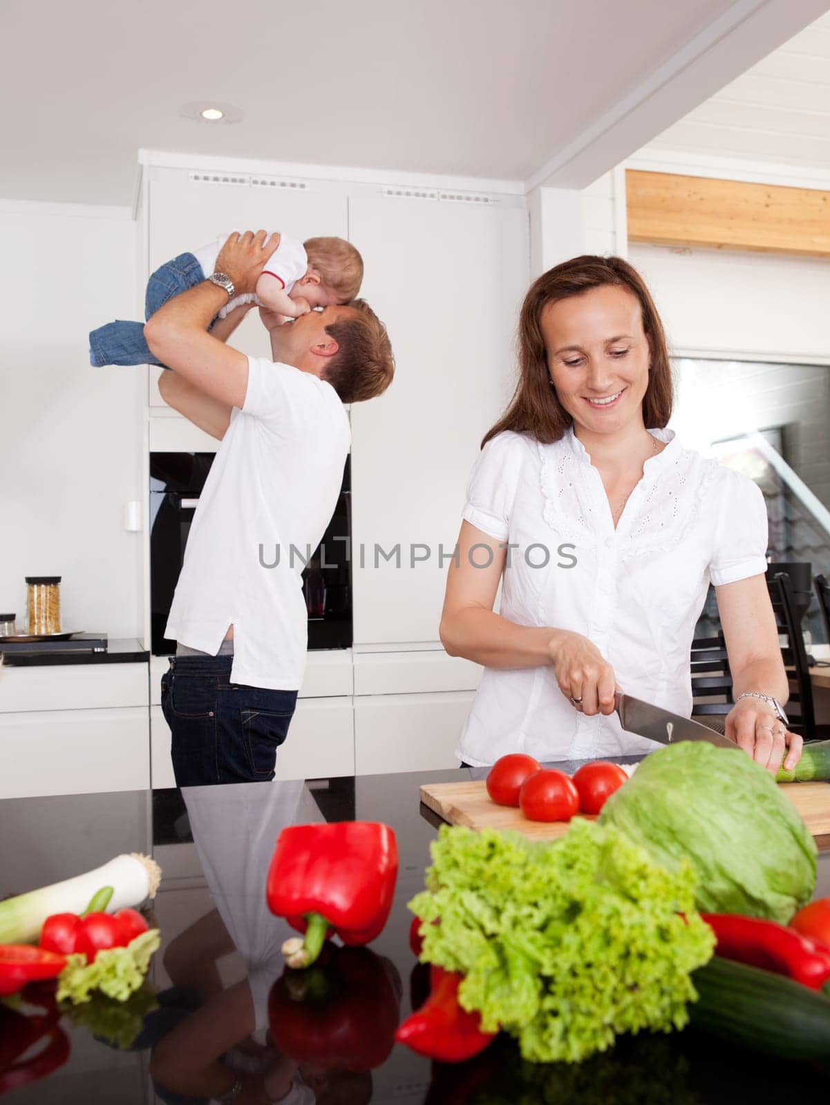 Happy family at home with mother making salad and father playing with son in background