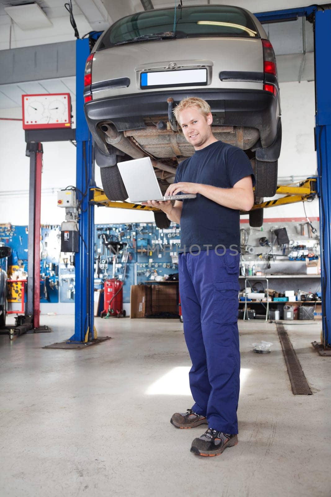 Full length portrait of smiling young mechanic using laptop in his auto repair shop