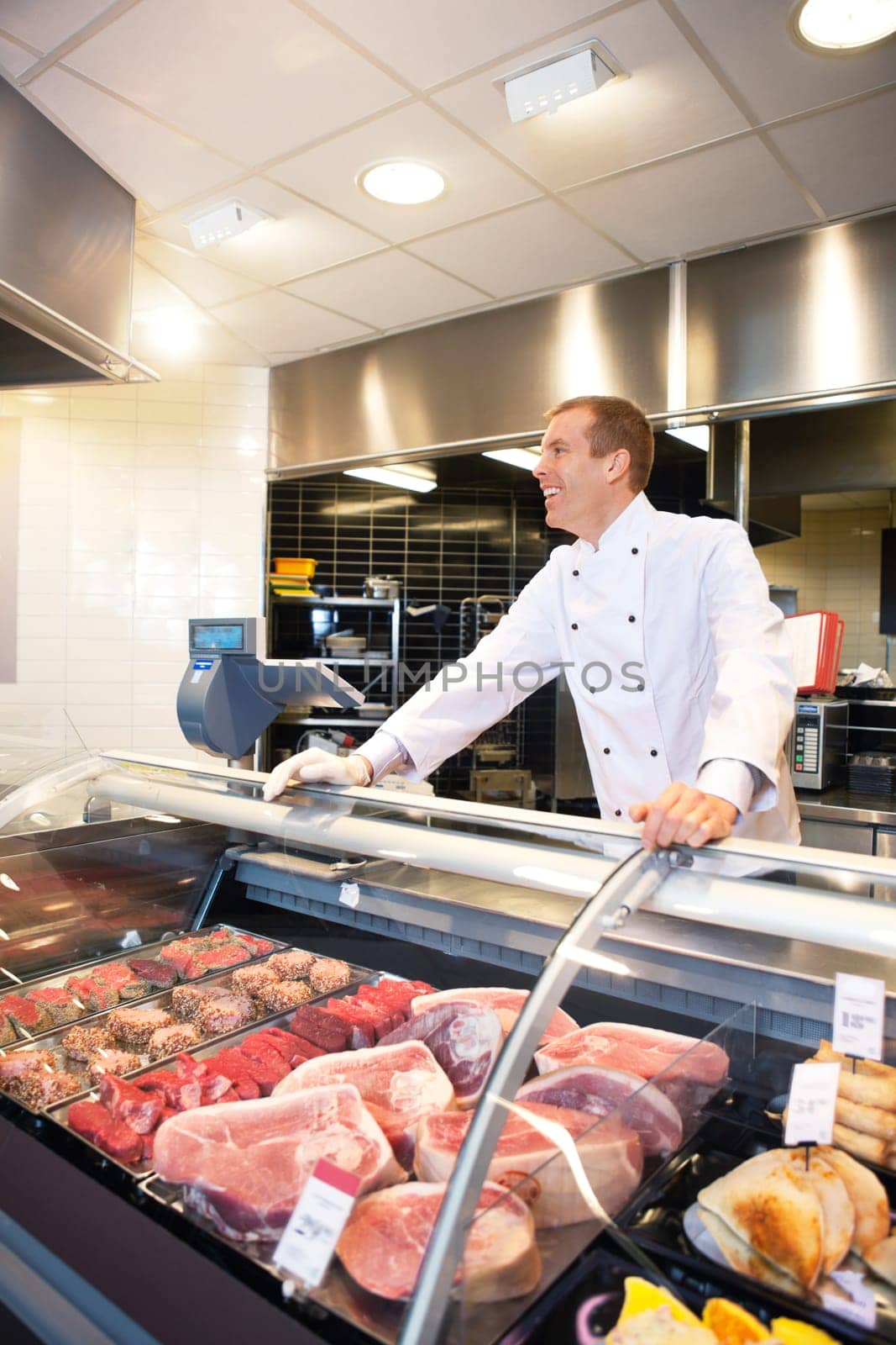 Cheerful chef on the counter of frozen meat in the supermarket