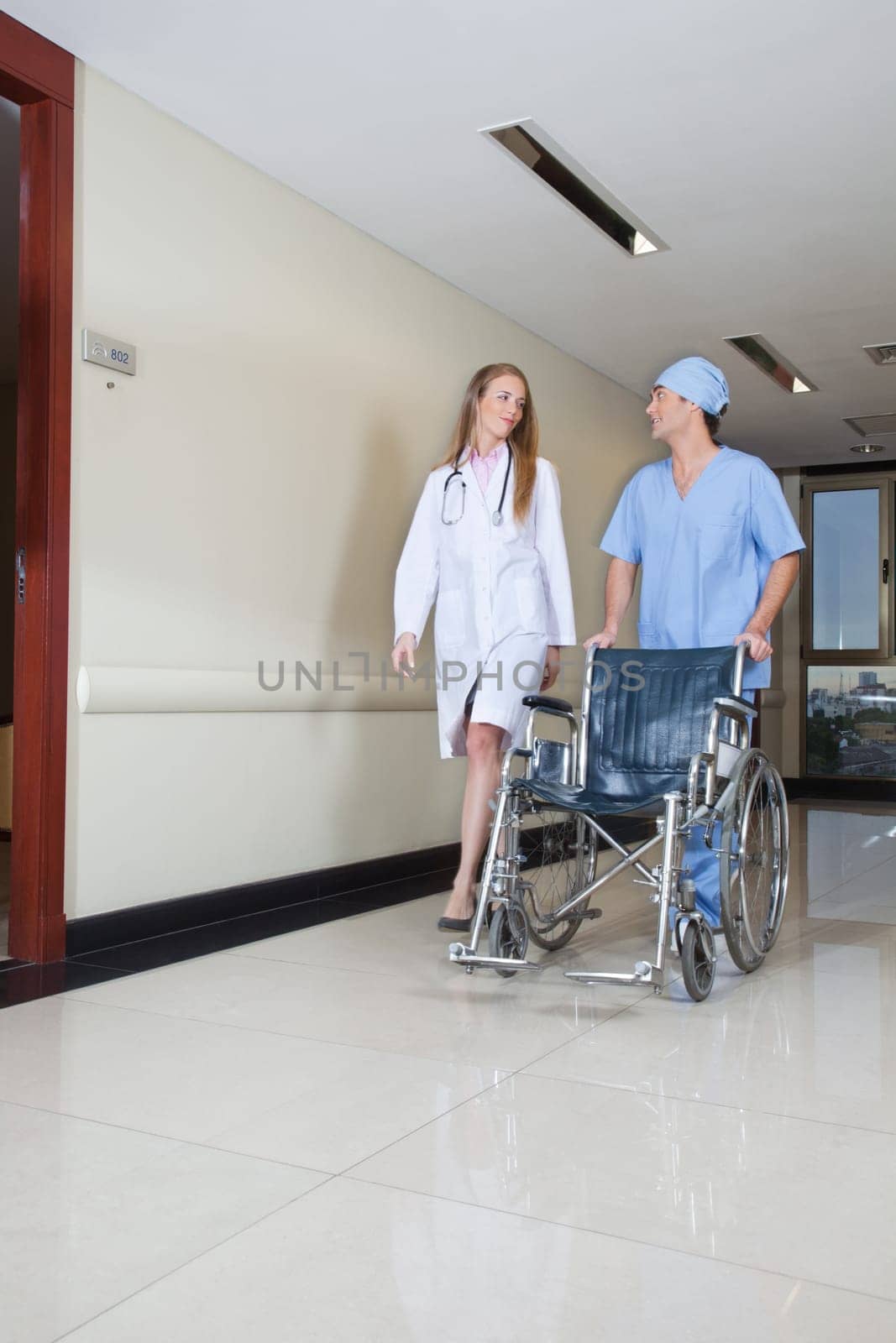 Doctor walking with male nurse pushing wheelchair