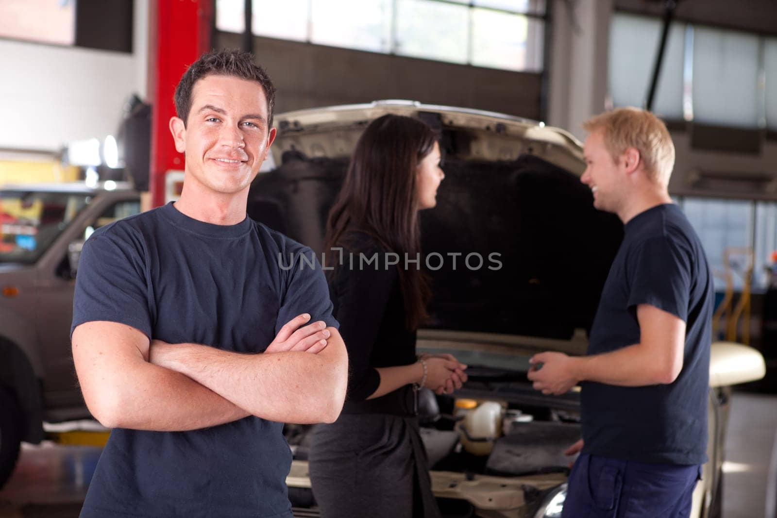 Portrait of a mechanic looking at the camera with a customer and second mechanic in the background