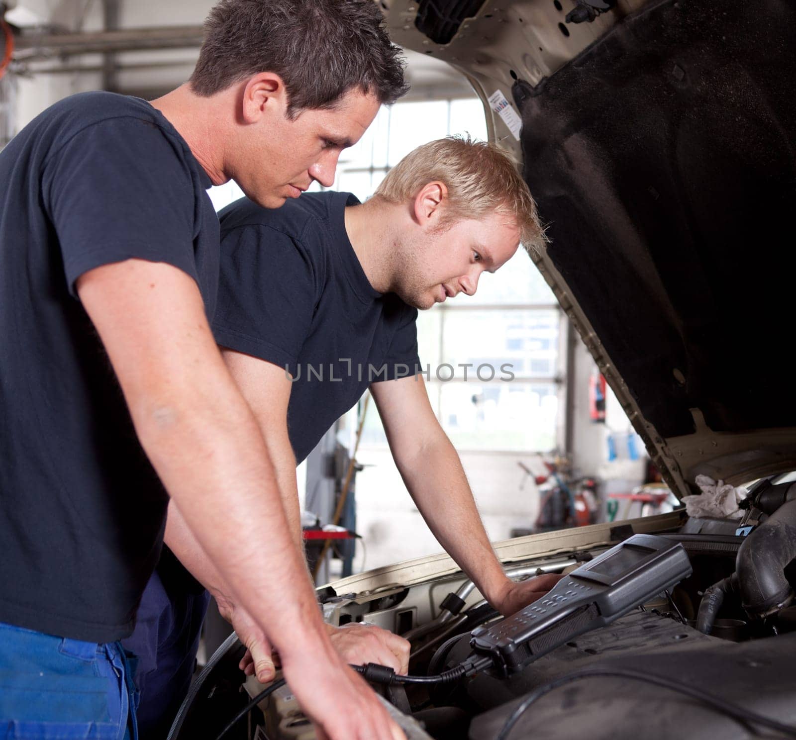 Two man mechanics looking a diagnostics equipment, servicing car