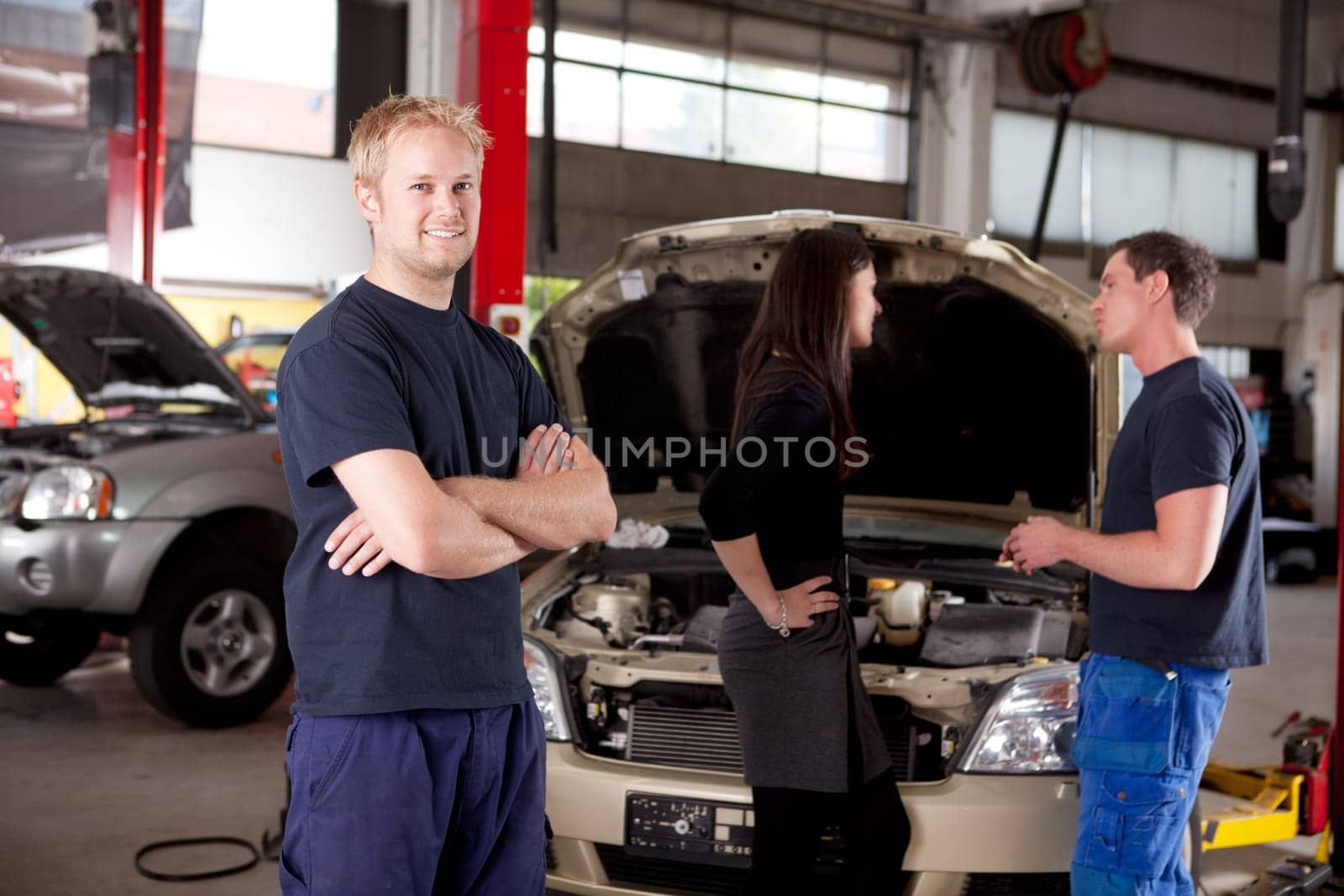 Mechanic looking at camera with customer and second mechanic in background