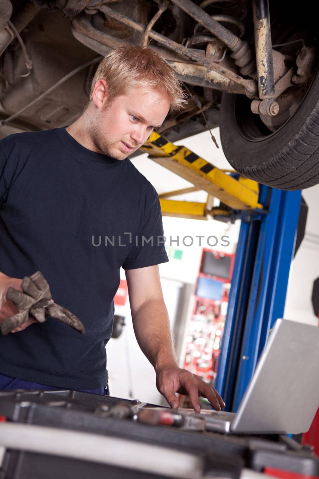 An automechanic referring to a laptop for the service order or manual