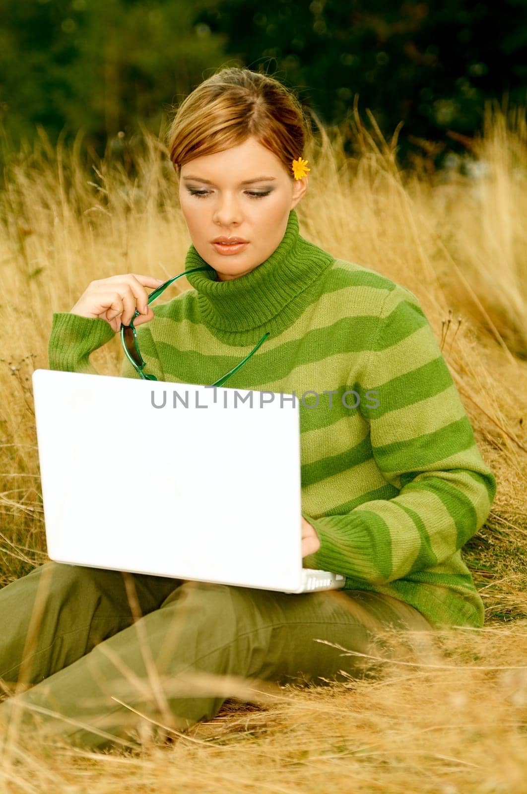 Young business woman working on laptop computer on golden meadow at mountains outdoors