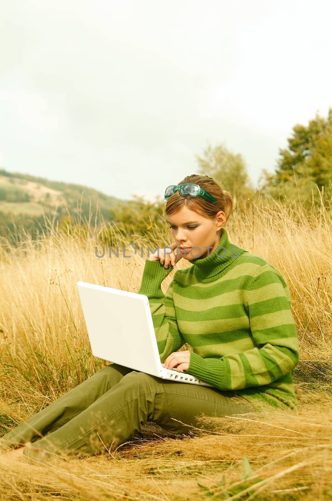 Young business woman working on laptop computer on golden meadow at mountains outdoors