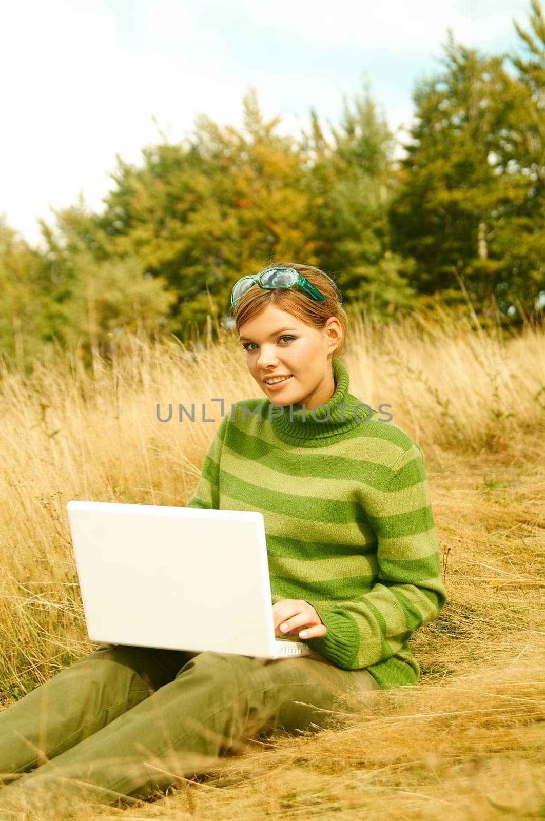 Young business woman working on laptop computer on golden meadow at mountains outdoors