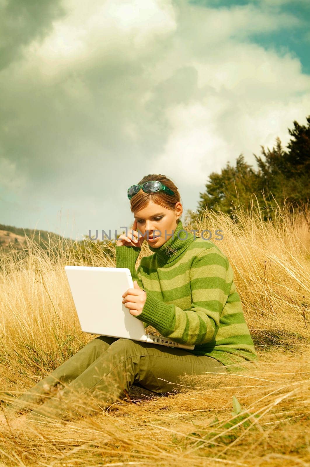 Young business woman working on laptop computer on golden meadow at mountains outdoors