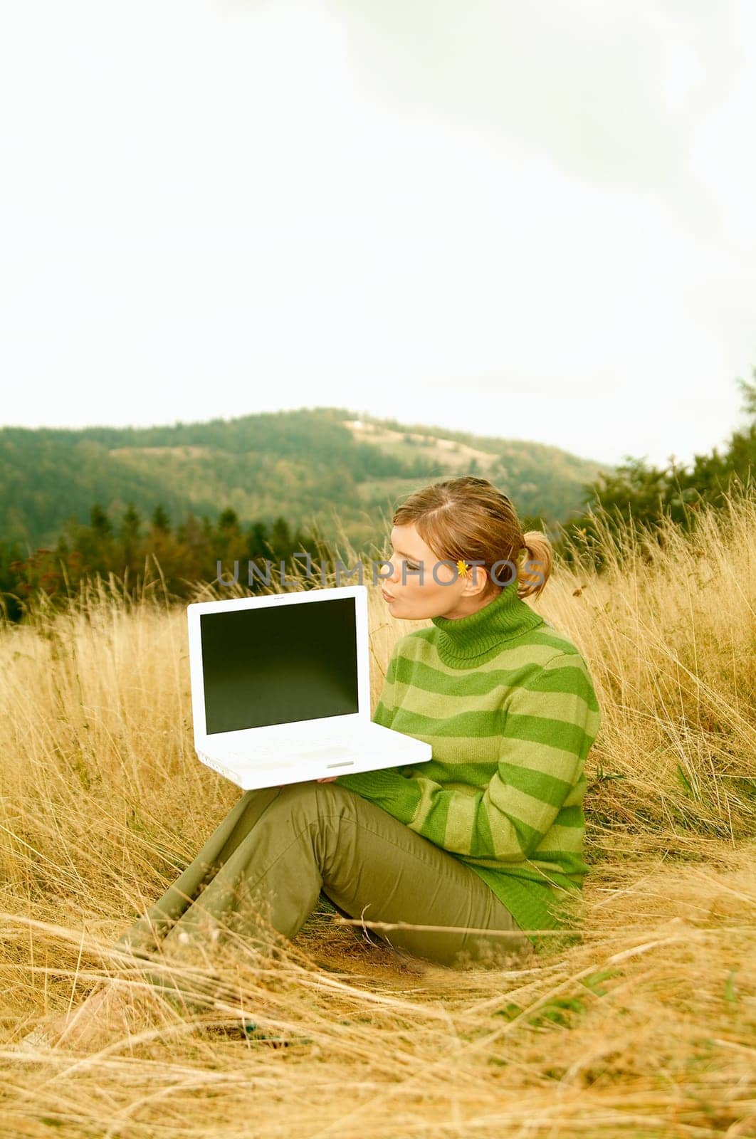 Young business woman holding laptop computer on golden meadow at mountains outdoors