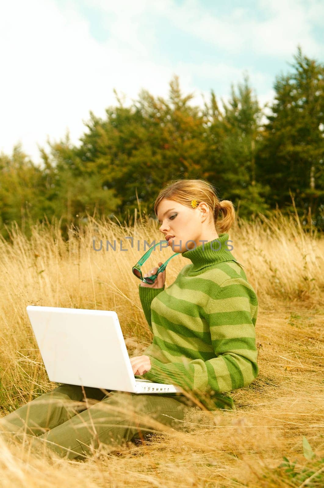 Young business woman working on laptop computer on golden meadow at mountains outdoors