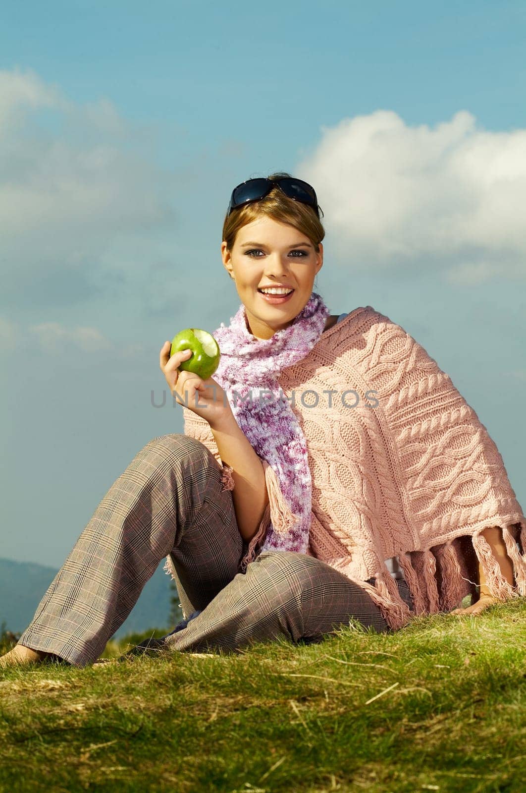 Young business woman relaxing on meadow, holding green fresh apple