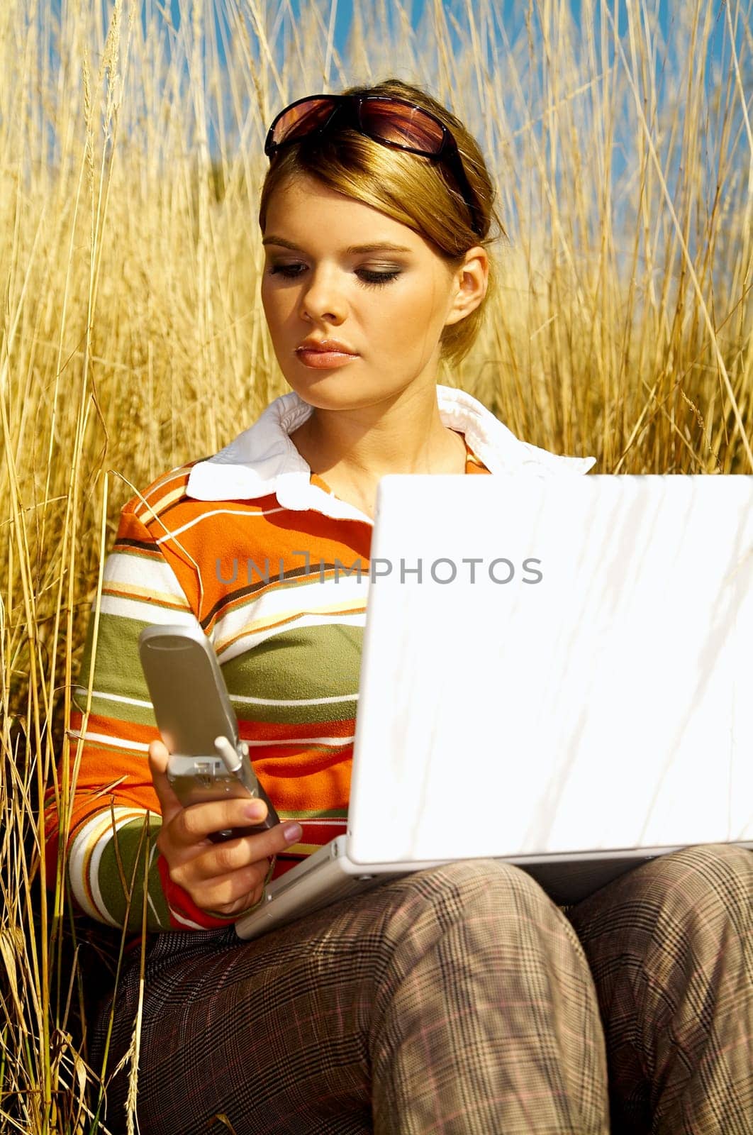 Young business woman relaxing, working on laptop computer and talking cell phone on meadow