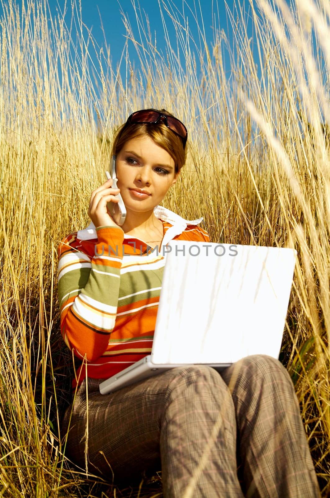 Young business woman relaxing, working on laptop computer and talking cell phone on meadow