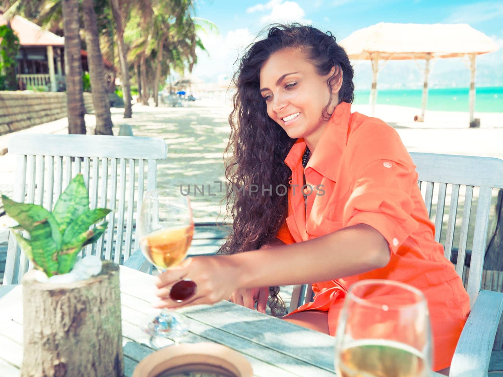 Young woman with glass of wine has a dinner on the beach