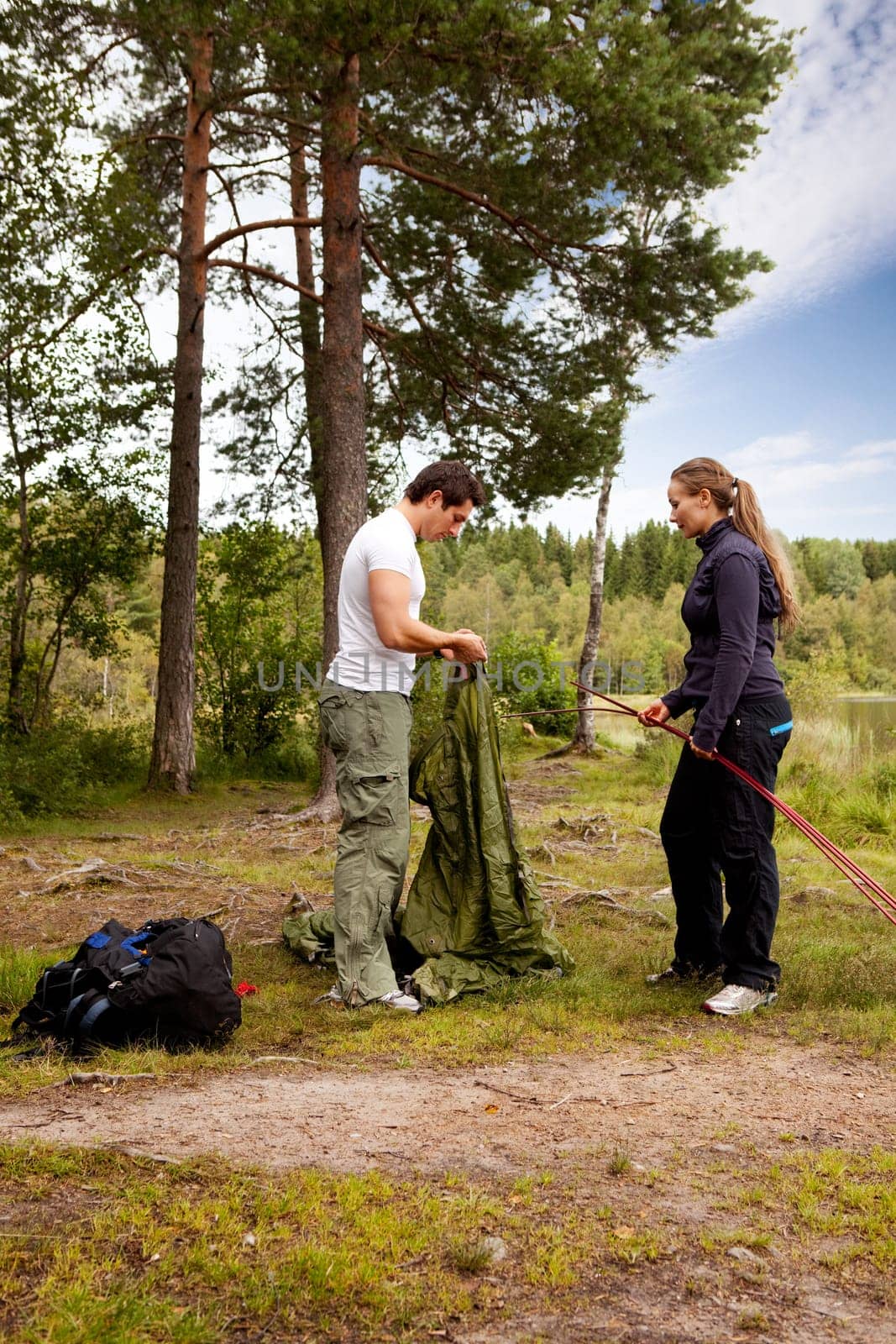 Camping lifestyle - a man and woman setting up a tent by a lake