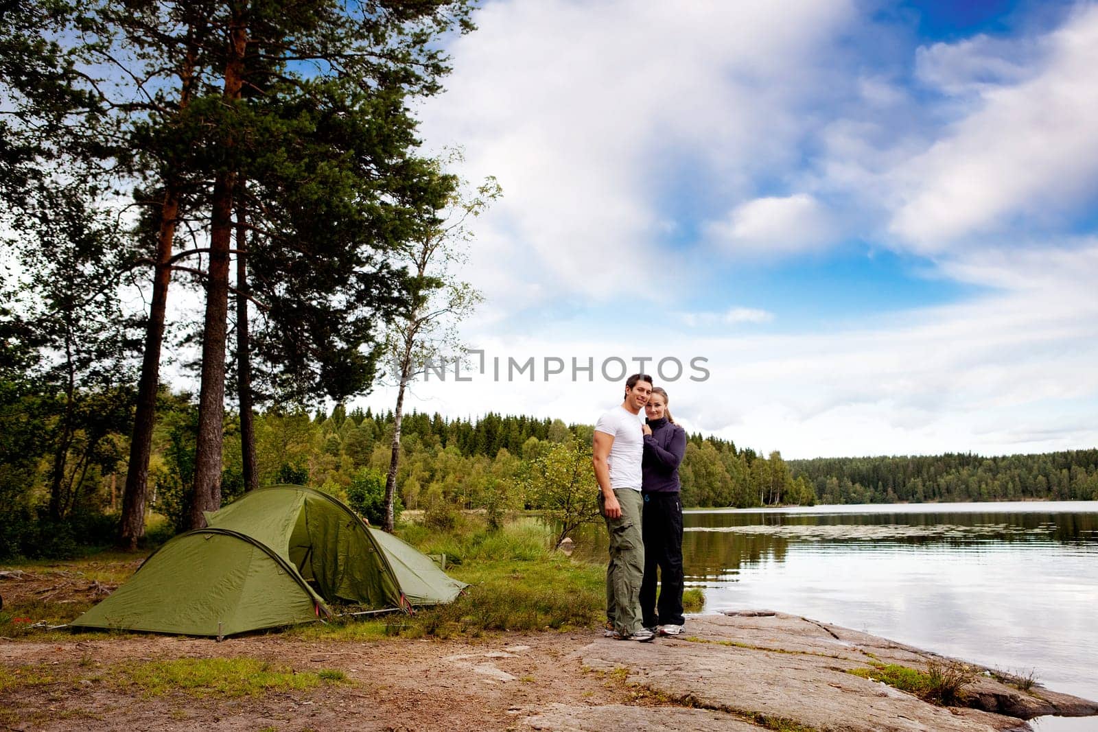 A couple of happy campers by a lake and forest