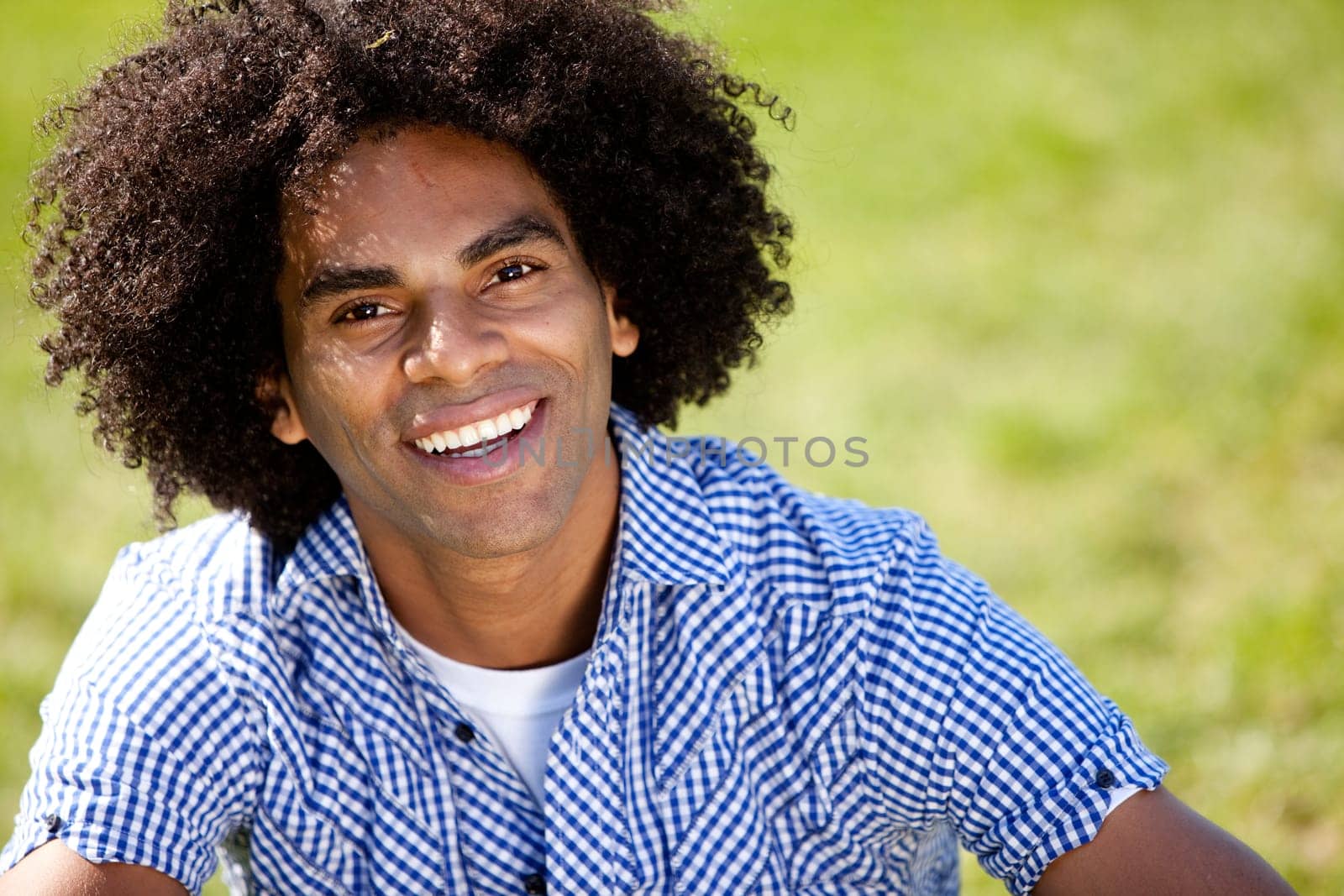 Young man smiling at camera in a park. Horizontally framed shot.