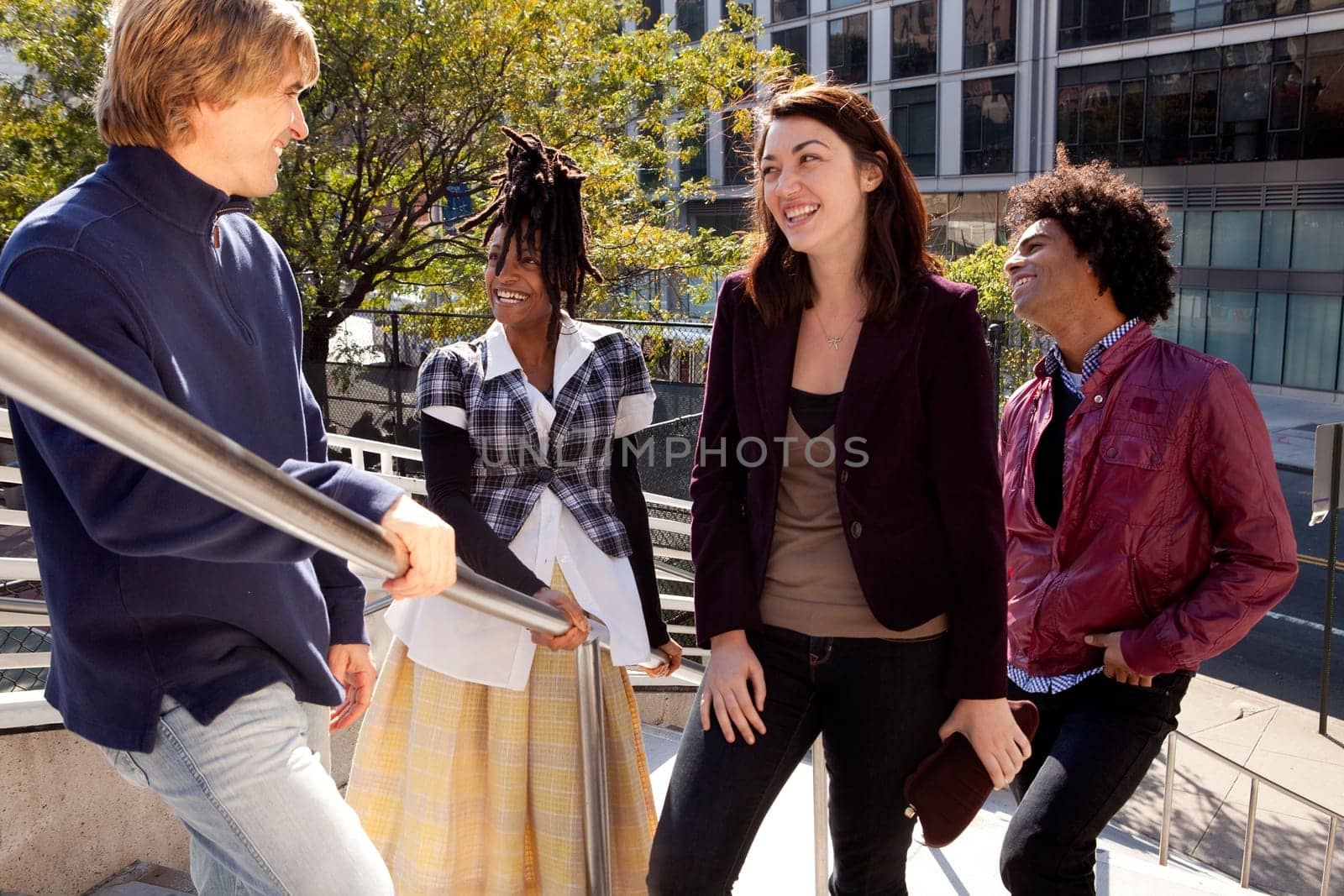 Group of four people of different ethnicities standing by stair railing. Horizontally framed shot.