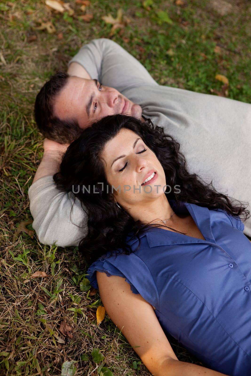 A couple laying on grass in a park daydreaming.  Focus on the womans eyes