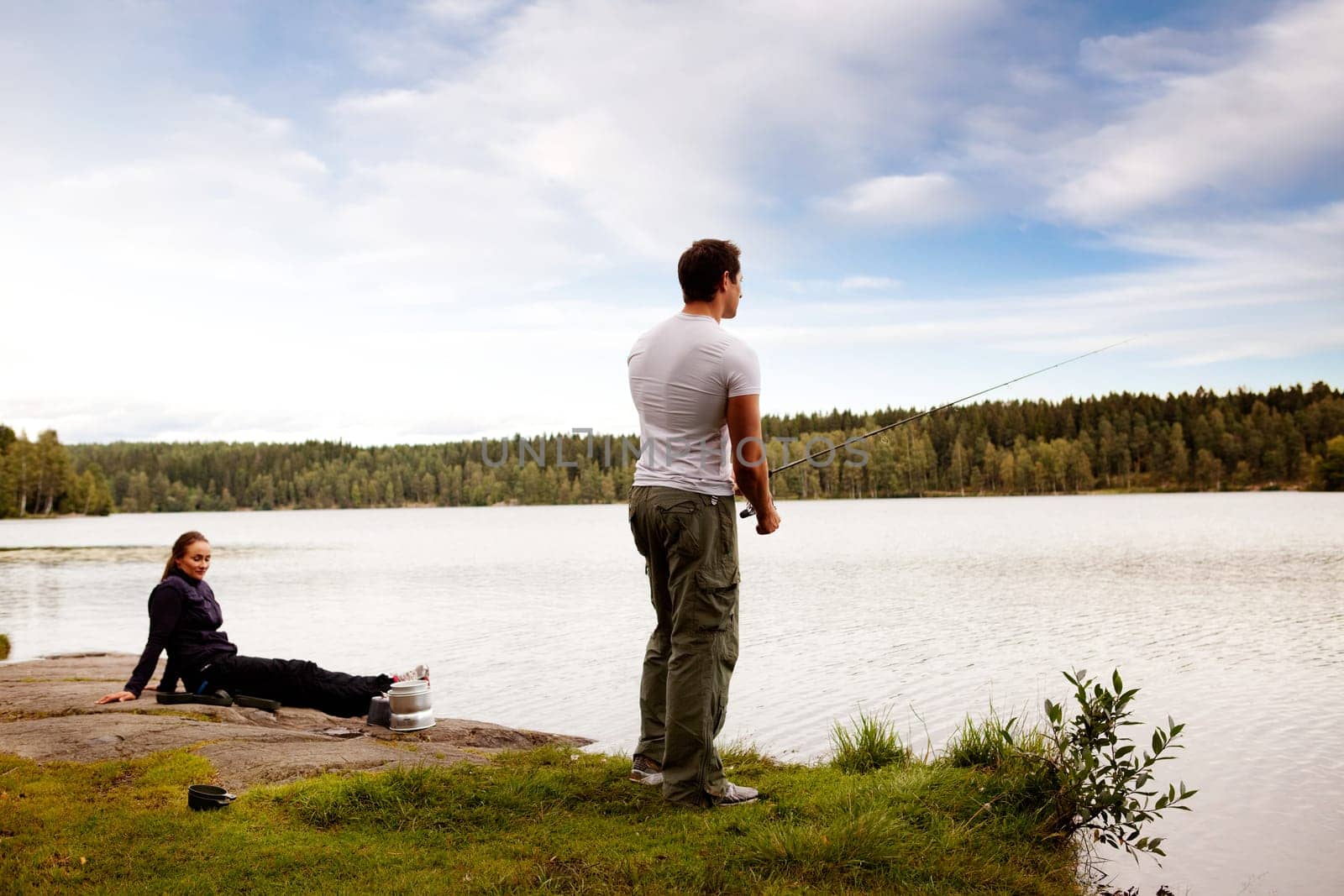 A man fishing on a forest lake with woman in the background