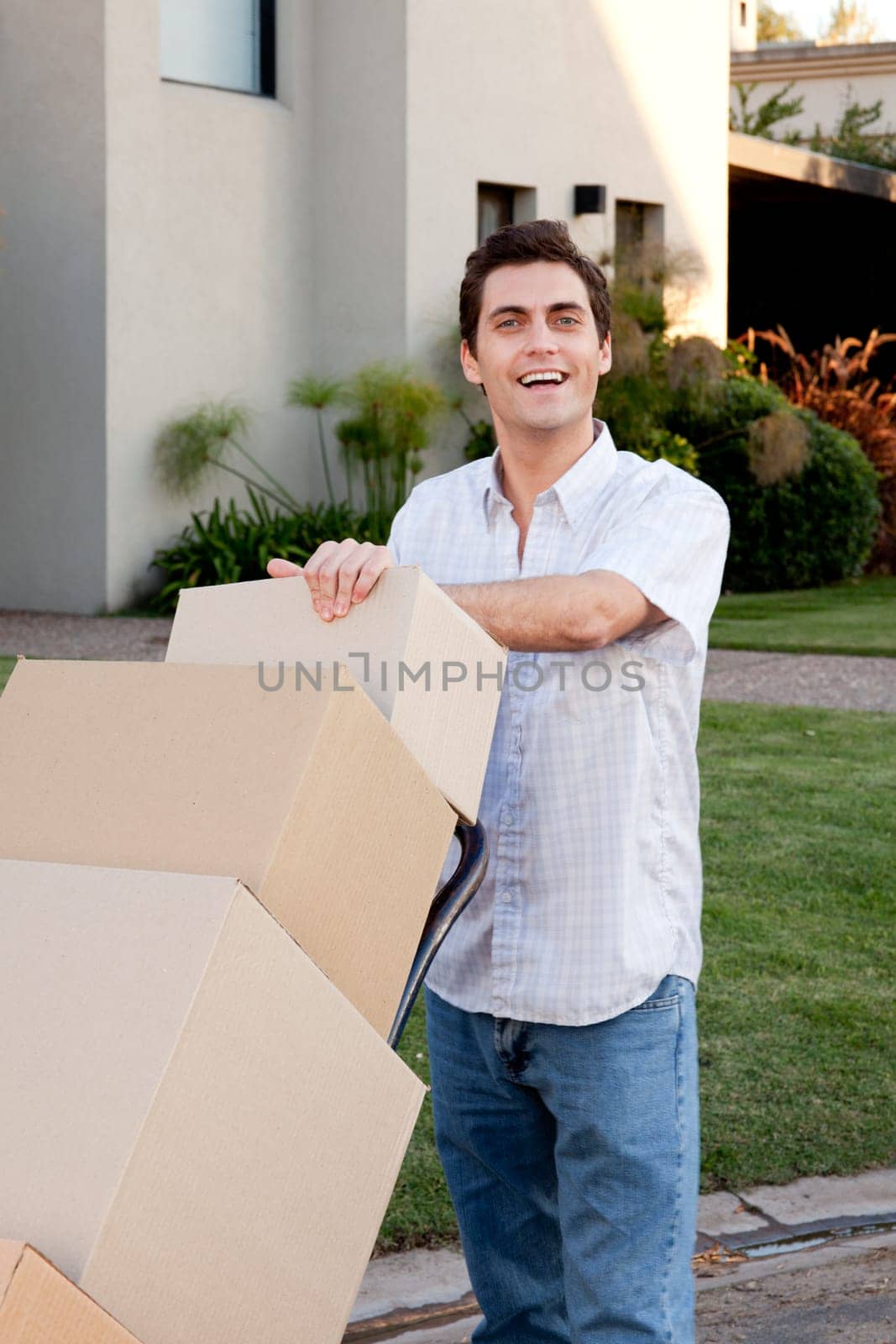 A happy male looking at the camera pushing a dolly with moving boxes