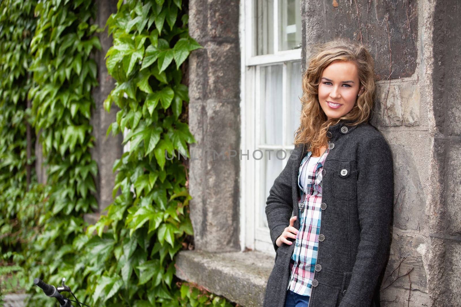 Confident young blond woman smiling an leaning against stone wall