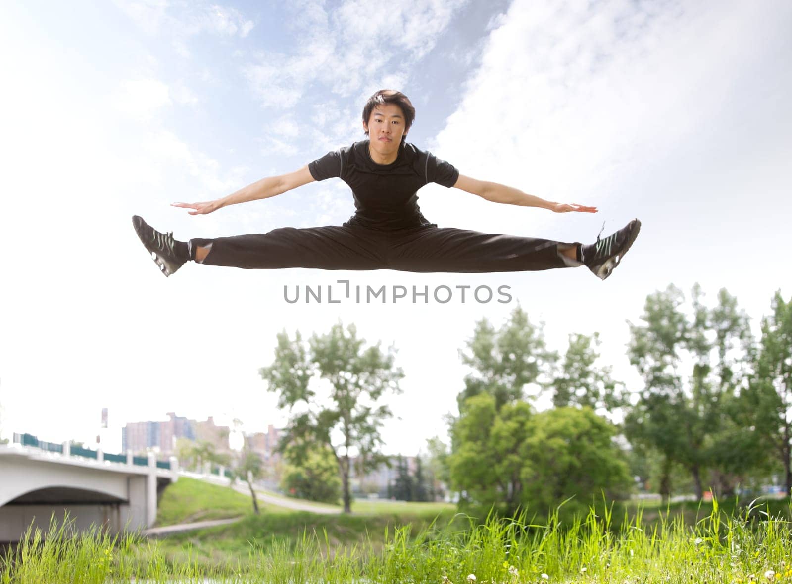 Young man jumping in the air near bridge under clear sky