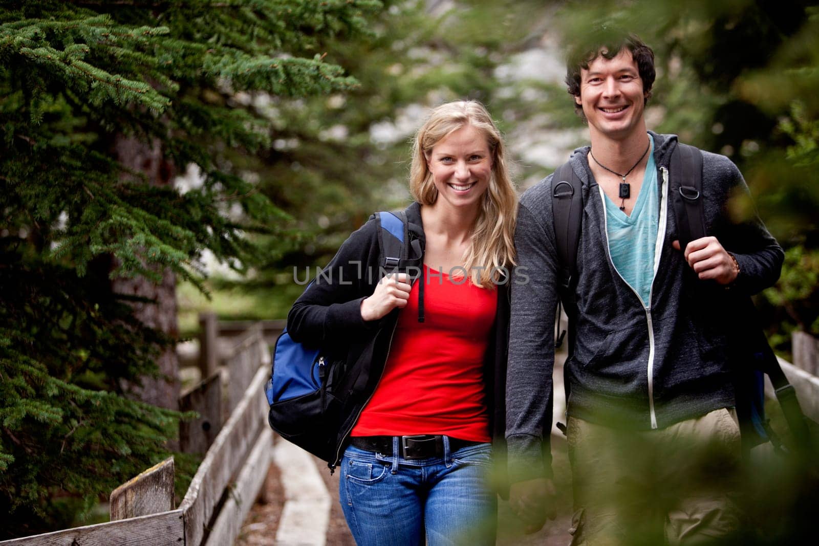 A man and woman on a hike in the forest, smiling at the camera